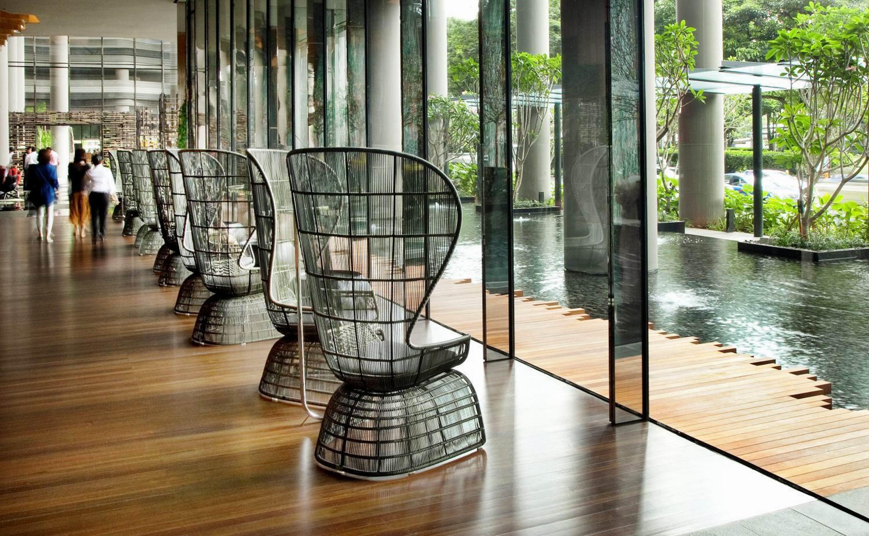 Parkroyal Collection Pickering, Сингапур Екстериор снимка The photo features a modern interior space with large glass windows that allow natural light to flood in. Along one side of the room, there are several distinctive black chairs with an open, lattice-like design. The flooring is made of polished wood,