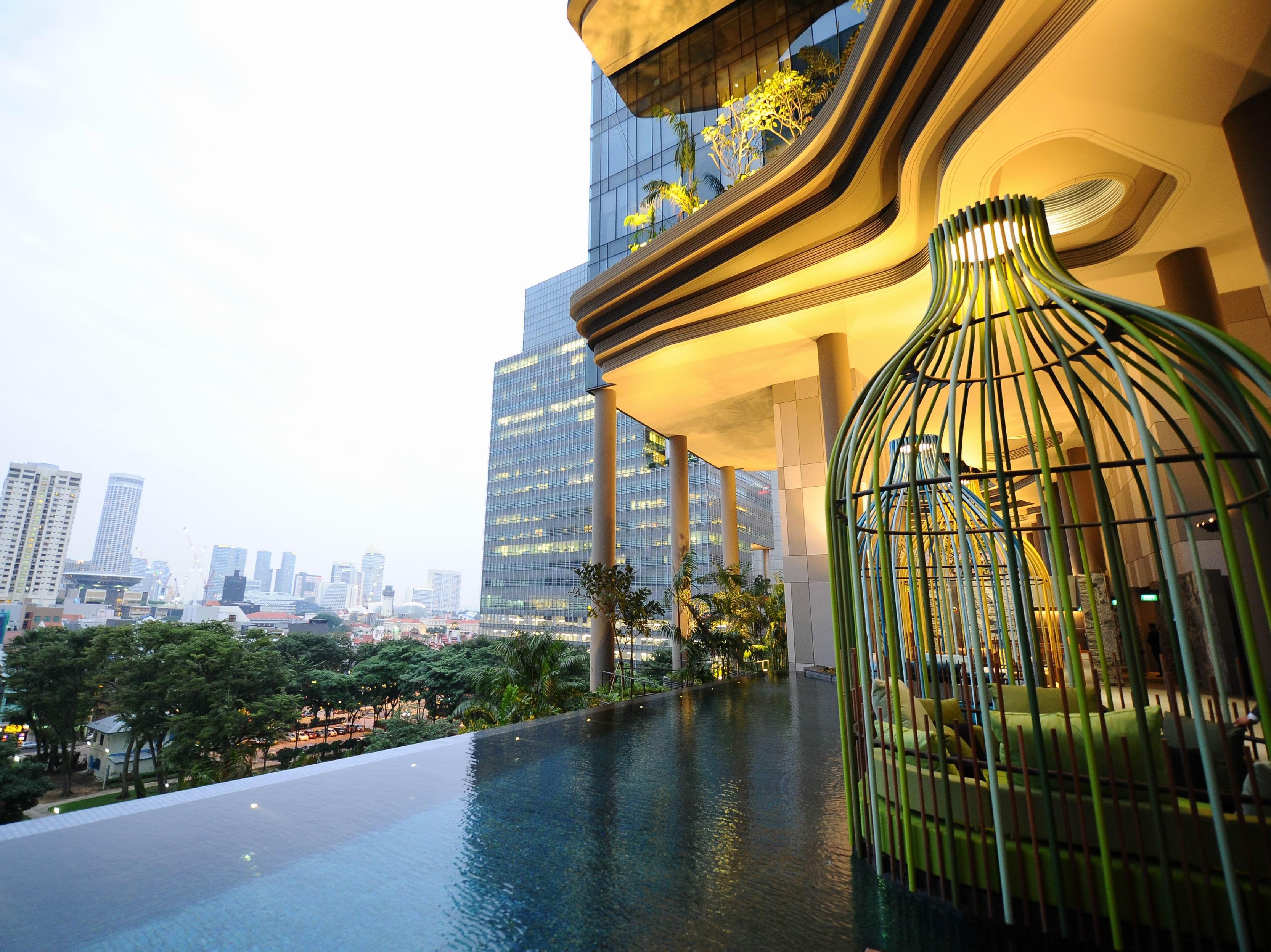 Parkroyal Collection Pickering, Сингапур Екстериор снимка The photo showcases a modern, luxurious space that features an infinity pool with a sleek, reflective surface. In the foreground, there is a unique structure resembling a large birdcage, designed with green elements. The background includes tall city