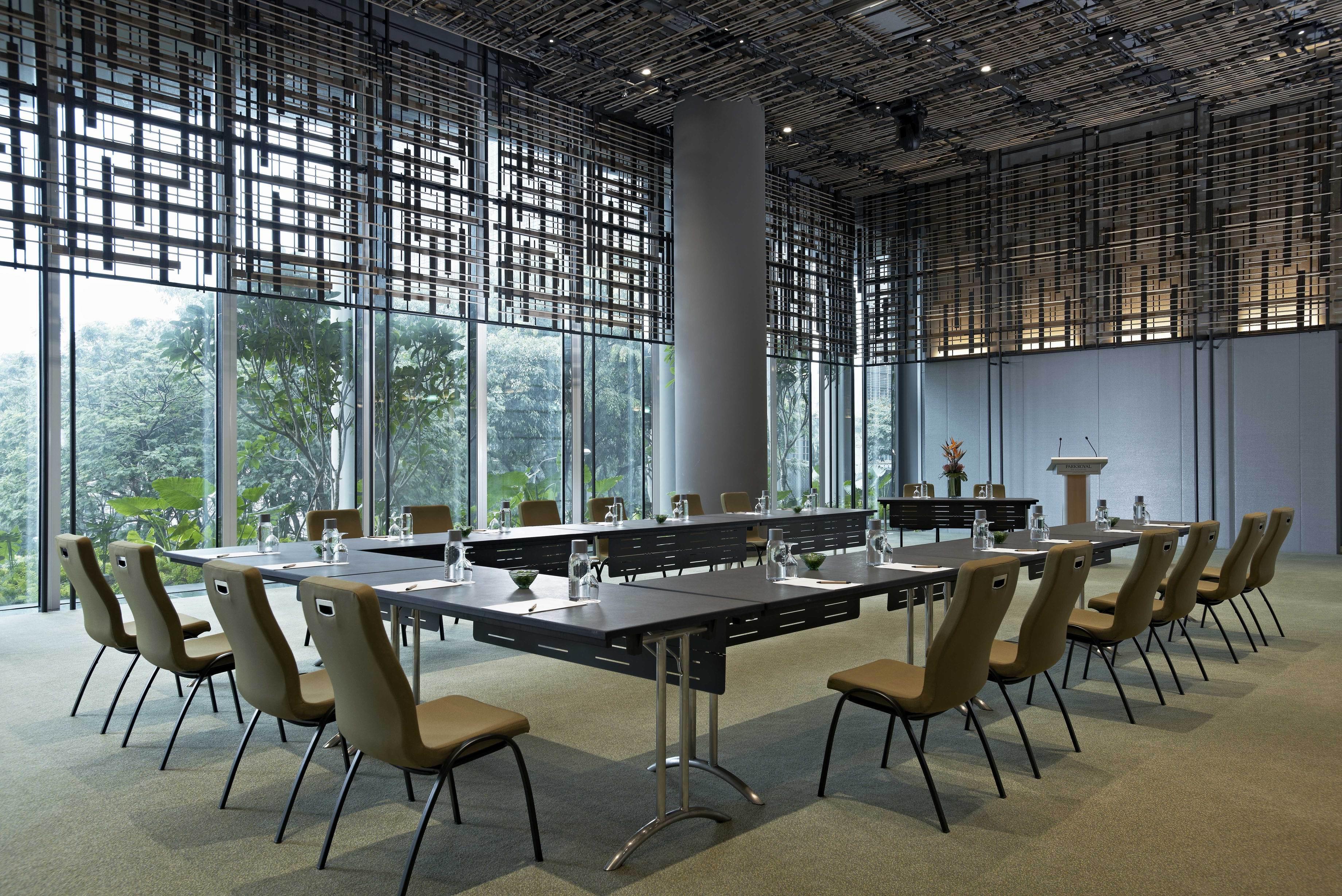 Parkroyal Collection Pickering, Сингапур Екстериор снимка The image shows a modern conference room. It features a long, rectangular table surrounded by several chairs. The table is equipped with glass water bottles and glasses. Large windows provide natural light and offer a view of greenery outside. The ro