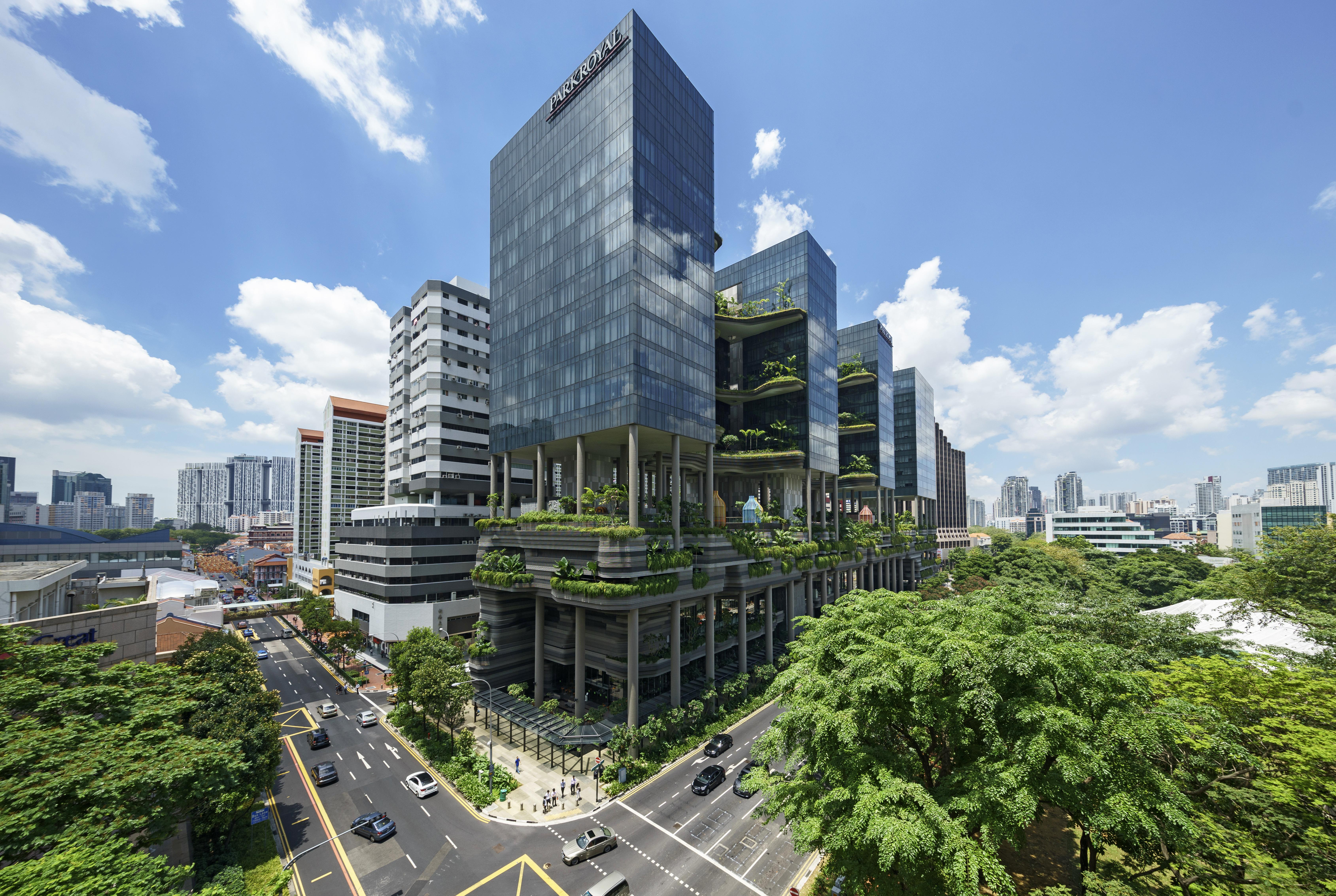 Parkroyal Collection Pickering, Сингапур Екстериор снимка The photo shows a modern urban architecture scene featuring several sleek glass buildings. These structures are complemented by greenery, with plants and trees integrated into their design, creating a lush environment. The scene includes a busy road 