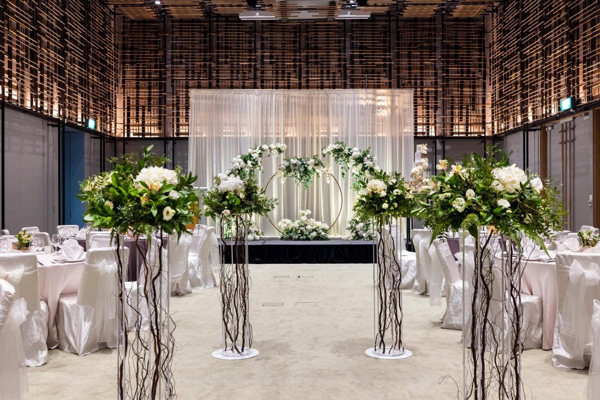 Parkroyal Collection Pickering, Сингапур Екстериор снимка The photo shows a beautifully decorated event space, likely set up for a wedding. In the center, there is an elegant backdrop made of draped fabric, creating a soft and romantic atmosphere. Flanking the backdrop are floral arrangements positioned on 
