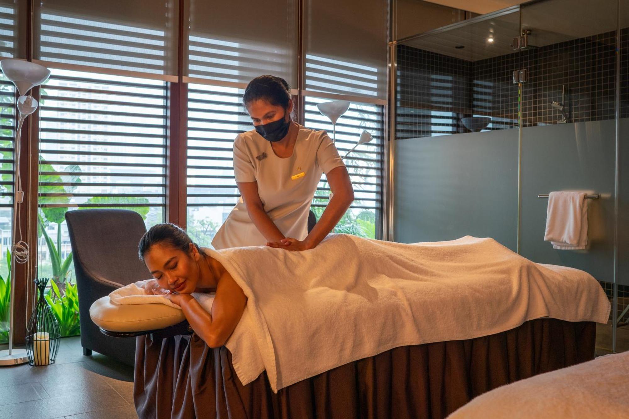 Parkroyal Collection Pickering, Сингапур Екстериор снимка The photo shows a serene spa setting where a therapist is giving a massage to a client. The client is lying face down on a massage table, covered with a towel, and appears to be relaxed. The therapist is positioned at the client's back, providing the