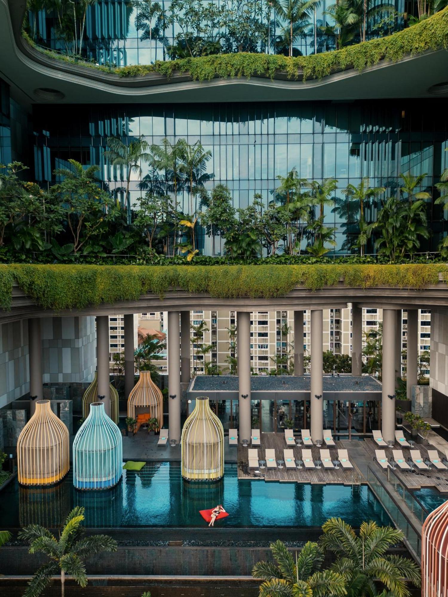 Parkroyal Collection Pickering, Сингапур Екстериор снимка The photo depicts a modern architectural design featuring a multi-level space. In the foreground, there are colorful structures resembling birdcages, which could be seating areas or decorative elements. Beyond them, there is a pool area lined with su
