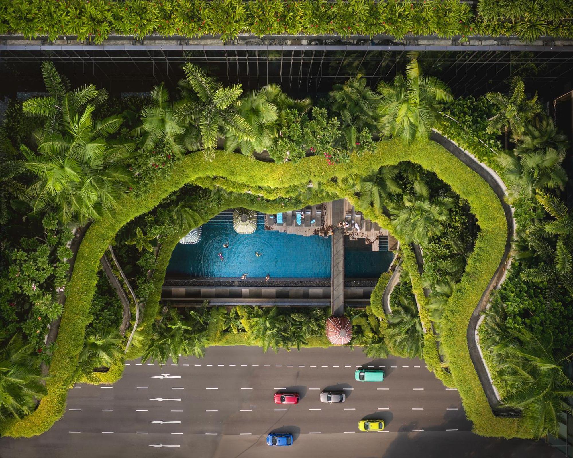 Parkroyal Collection Pickering, Сингапур Екстериор снимка The photo shows an aerial view of a green, lush landscape featuring a swimming pool surrounded by palm trees and other vegetation. The pool area is integrated into a modern architectural design, likely part of a hotel or resort, with paths and seatin