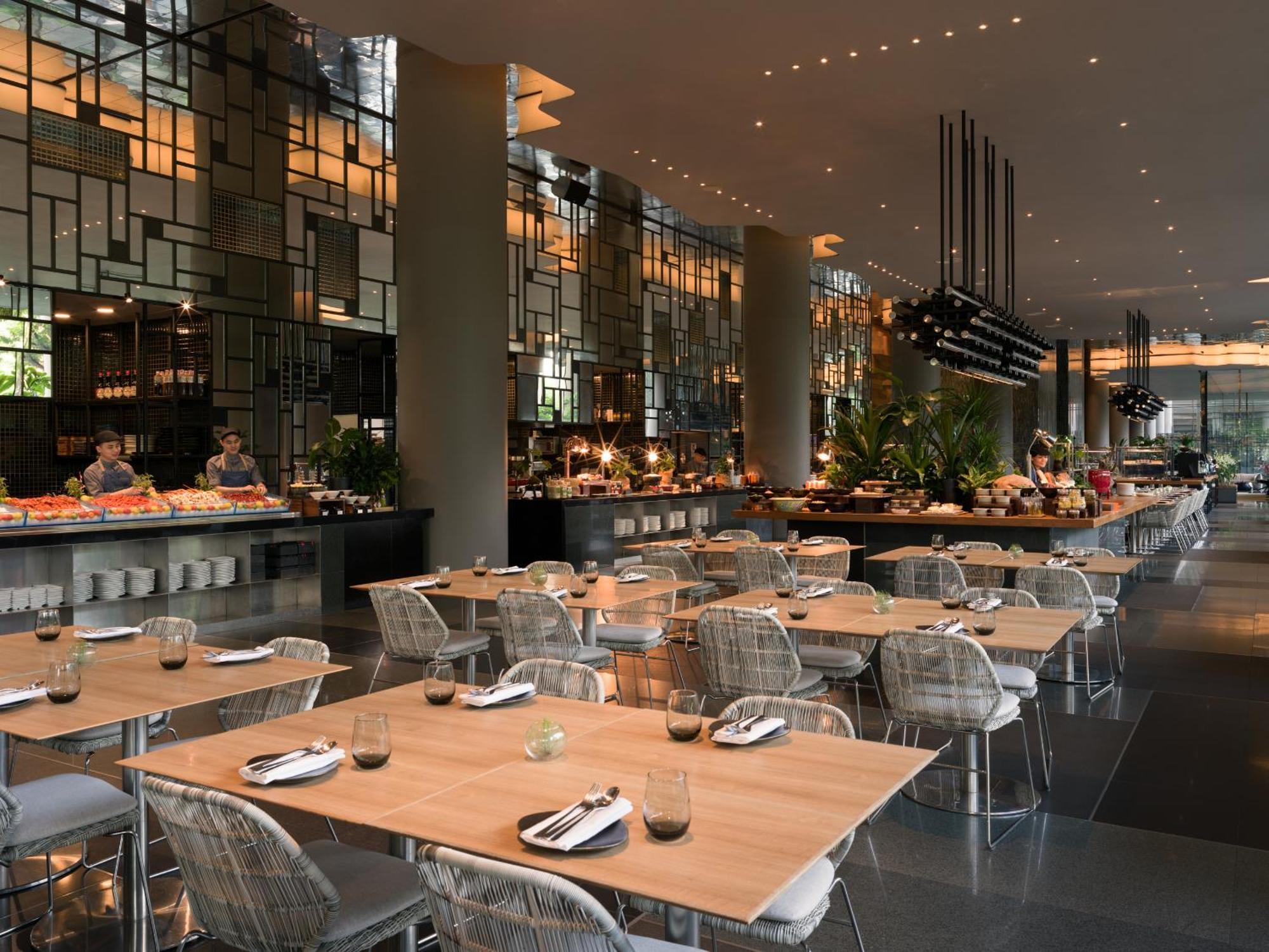 Parkroyal Collection Pickering, Сингапур Екстериор снимка The photo shows a modern restaurant interior with a spacious layout. There are several tables with wooden tops and transparent chairs arranged neatly. The design features large windows and stylish lighting, creating a warm ambiance. In the background